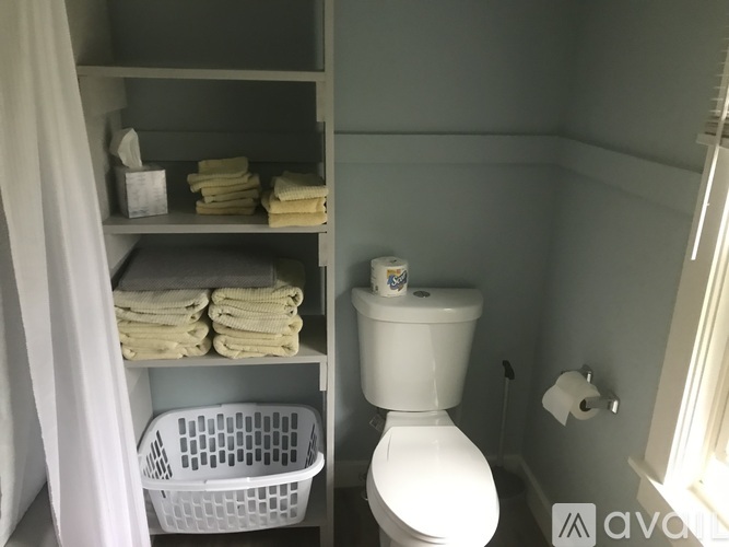 A bathroom with a toilet, towel shelf, and a basket.