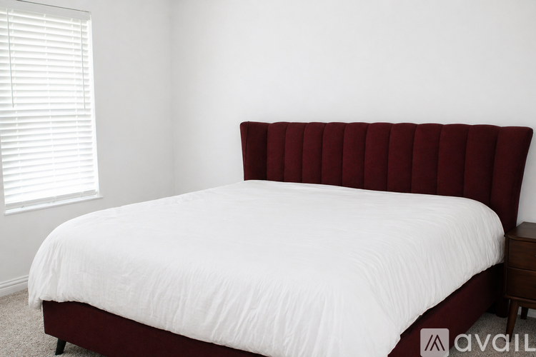 A bed with a white sheet and a red headboard is in the image.