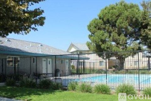 A pool is surrounded by a fence and a house is in the background.