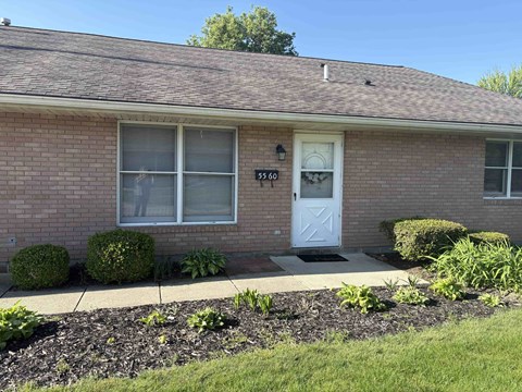 A house with a white door and windows with bushes in front.