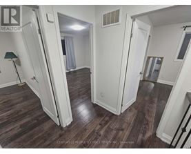A room with wood flooring and white walls, with a doorway leading to another room.
