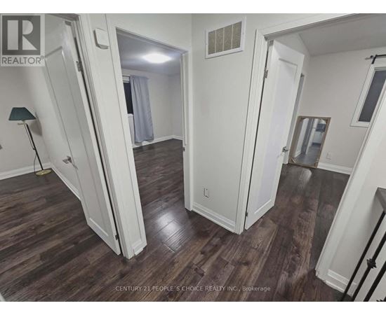 A room with wood flooring and white walls, with a doorway leading to another room.