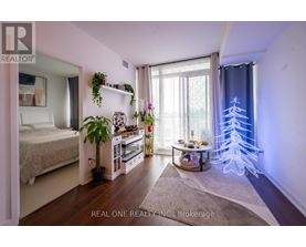 A bedroom with a bed, a table with a plant, and a window with a blue curtain.