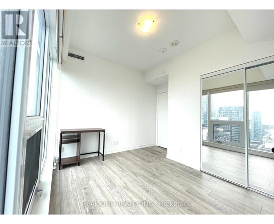 A spacious room with a wooden floor and a large window overlooking the city.