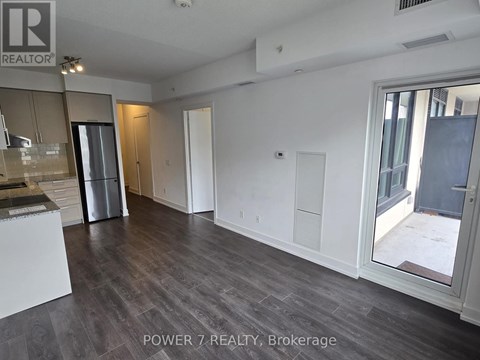 A spacious room with a kitchen area and a view of the outdoors through a glass door.