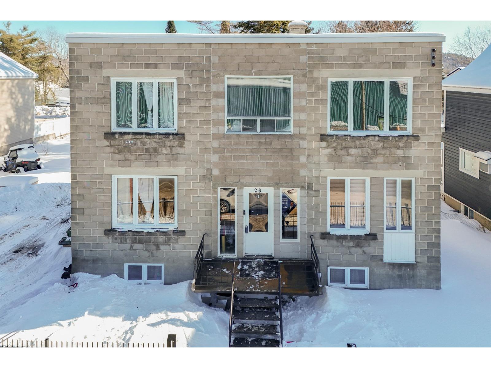 A house with a grey facade and white windows is surrounded by snow.