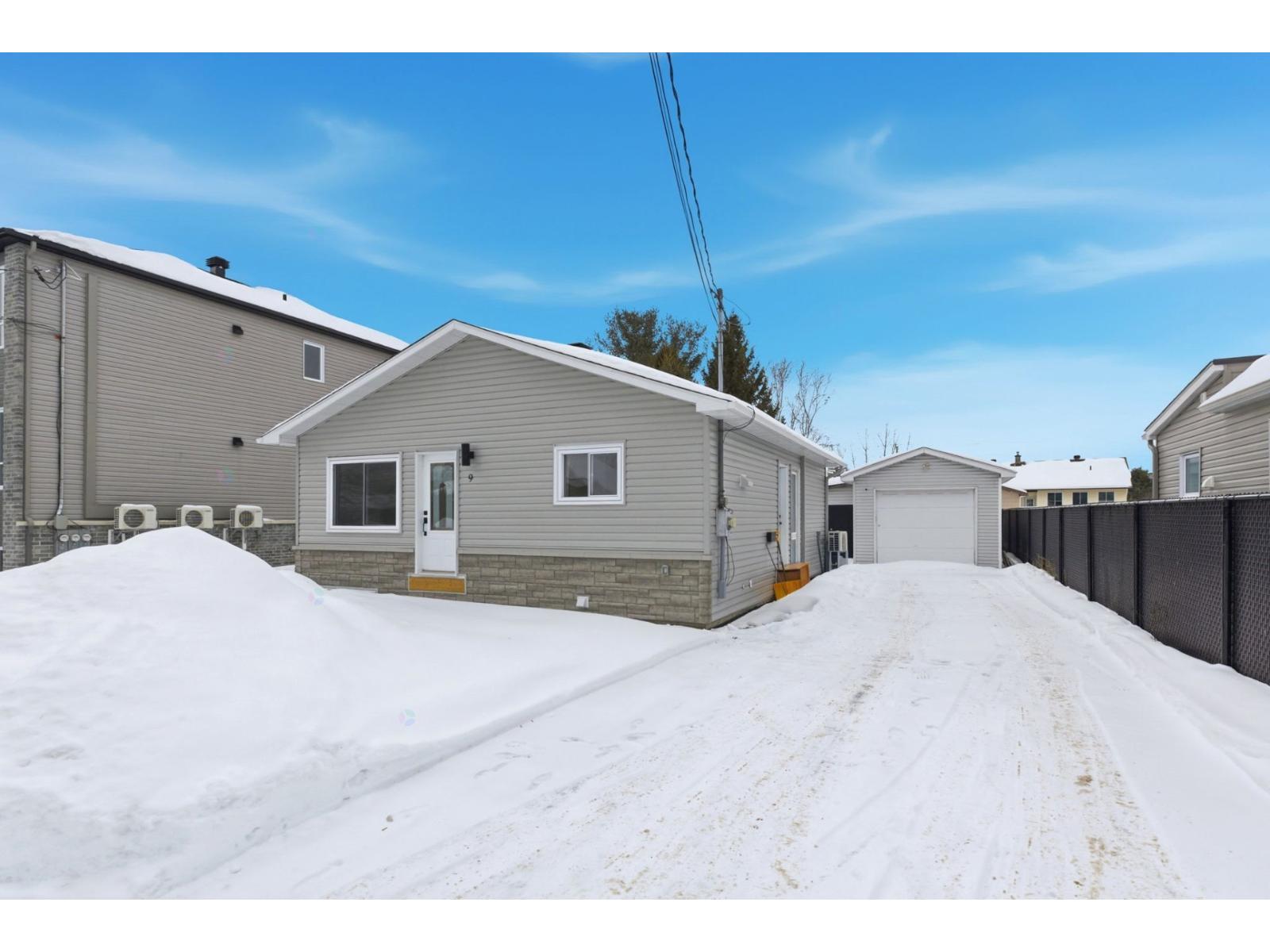 A snow-covered road leads to a house with a garage.