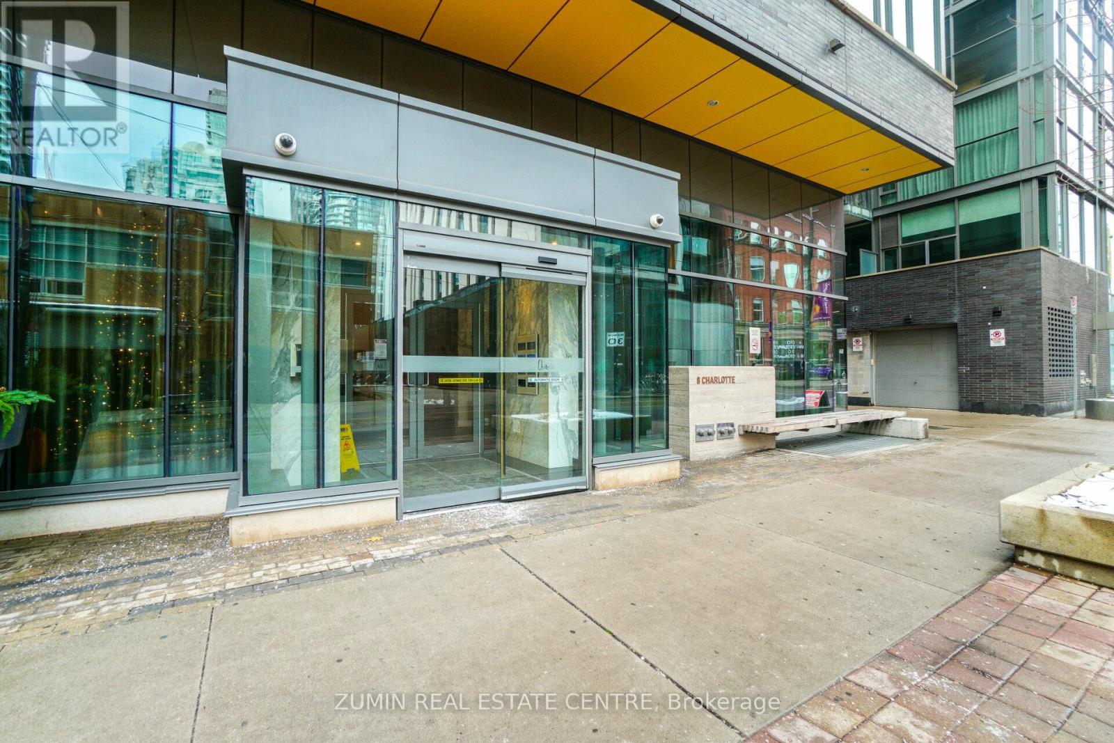 The image shows the front of the Zumin Real Estate Centre Brokerage building with large glass doors and windows.