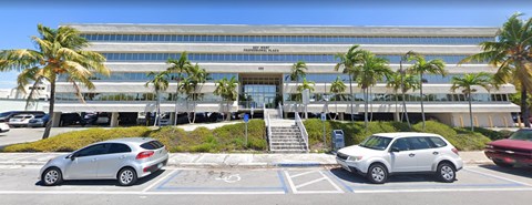 A white car is parked in front of a building with palm trees.