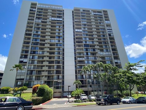 A tall residential building with a parking lot in front.