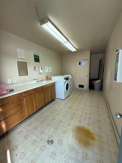 A dirty laundry room with a washing machine and a trash can.
