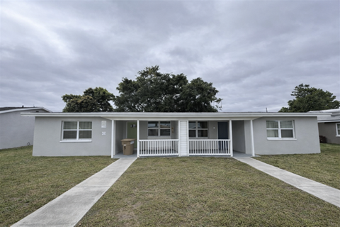 A grey house with a white fence and a green tree in the background.