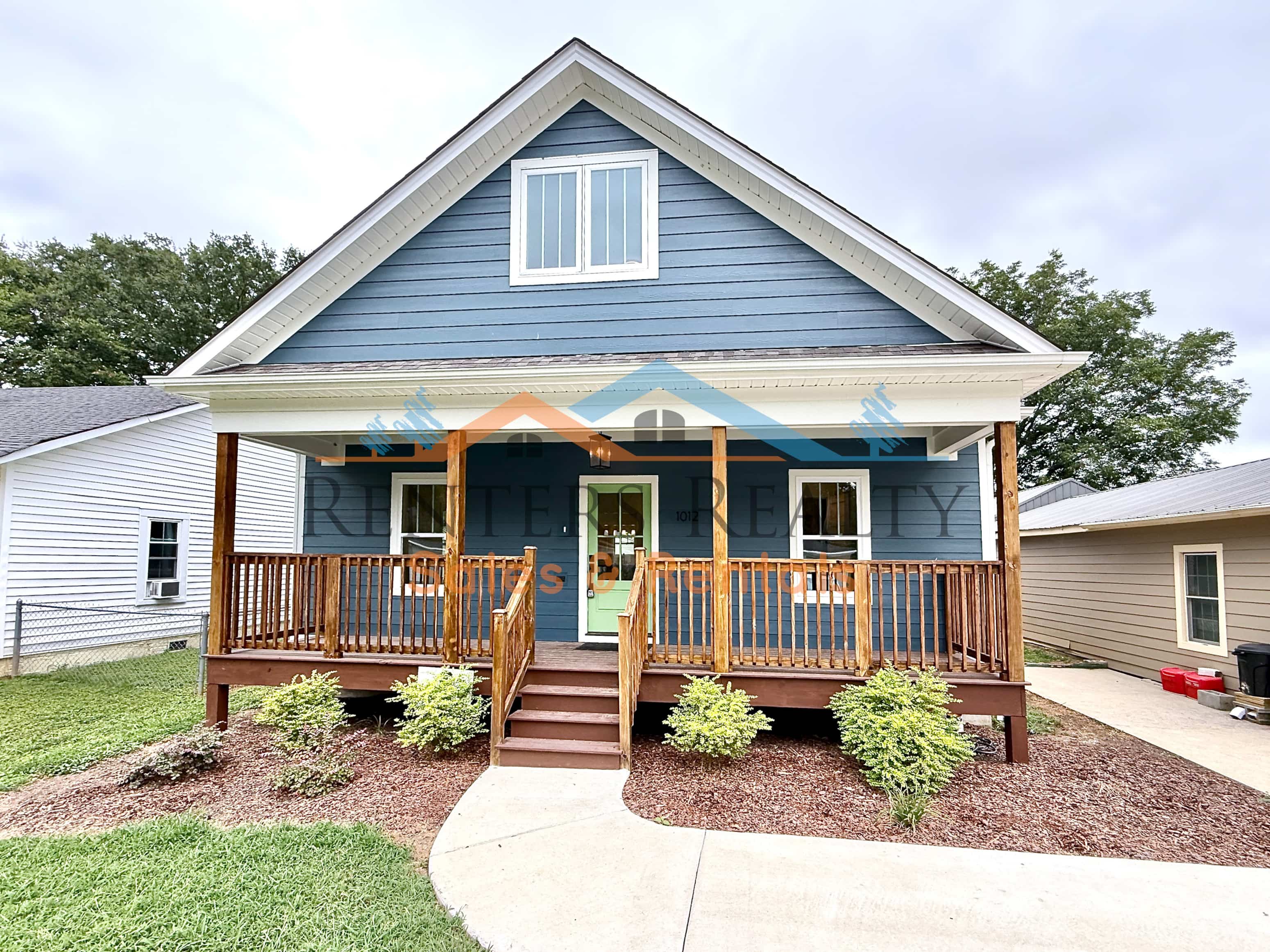 A blue house with a wooden porch and stairs leading to the front door.