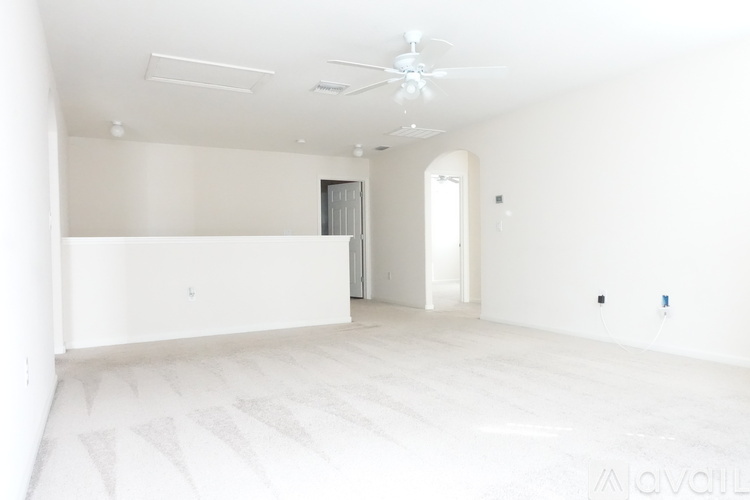 A spacious, empty room with a ceiling fan and a large white wall.