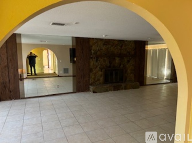 A man is standing in a spacious room with a stone fireplace.