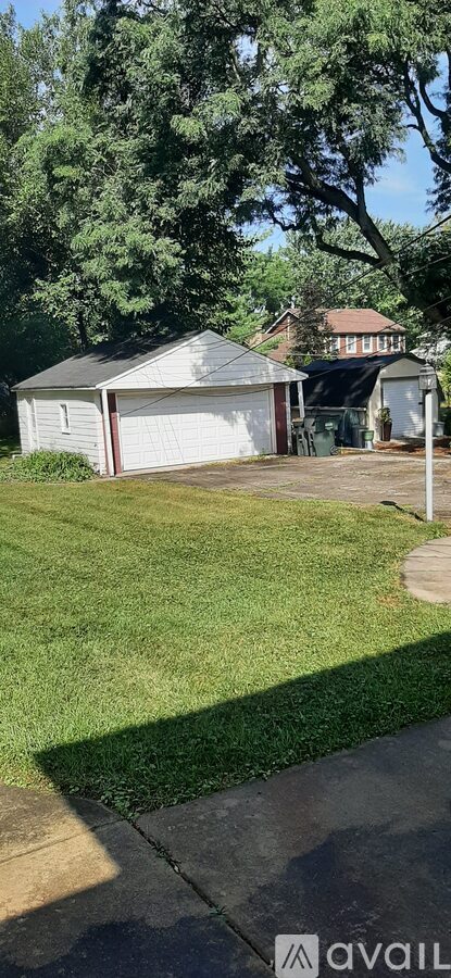 A white garage with a brown roof is surrounded by a green lawn and trees.