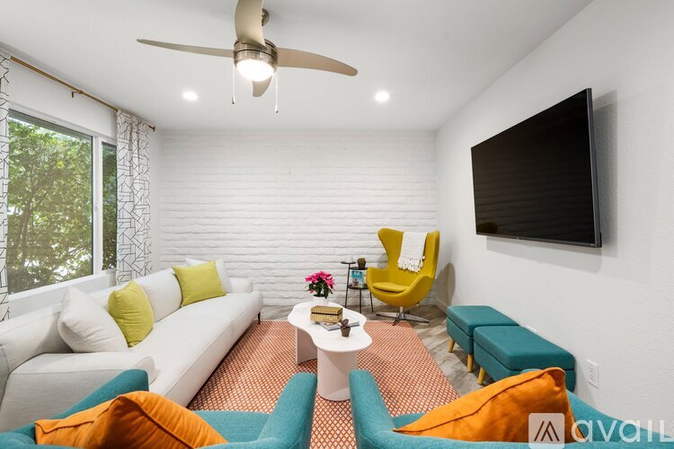 A living room with a white couch, a yellow chair, a white coffee table, and a flat screen TV mounted on the wall.