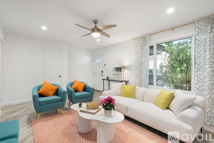 A living room with a white couch, two blue chairs, and a ceiling fan.