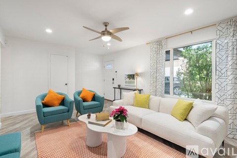 A living room with a white couch, two blue chairs, and a ceiling fan.
