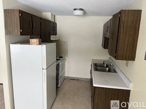 A small kitchen with a white refrigerator, a sink, and wooden cabinets.