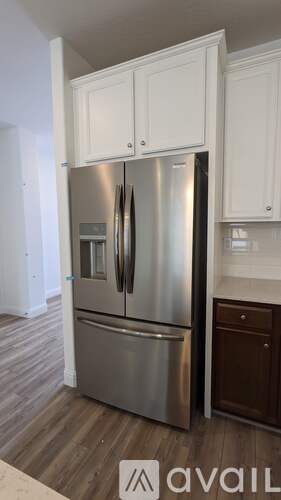 A stainless steel refrigerator with white cabinets above it.