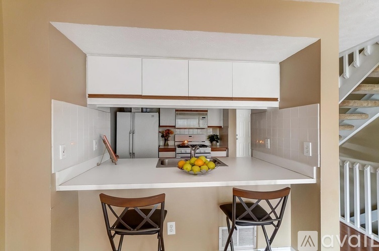A kitchen with white cabinets and a countertop with two chairs.