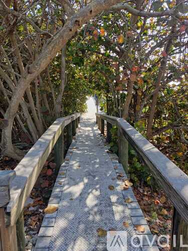 A wooden bridge with a metal railing and a tiled floor leads through a grove of trees.