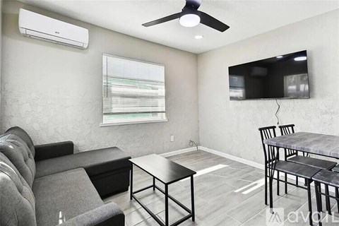 A living room with a grey couch, a black coffee table, and a television mounted on the wall.