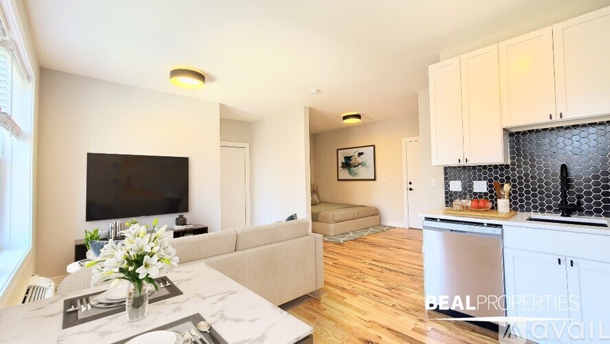 A modern living room with a flat screen TV and a kitchen area with a refrigerator.