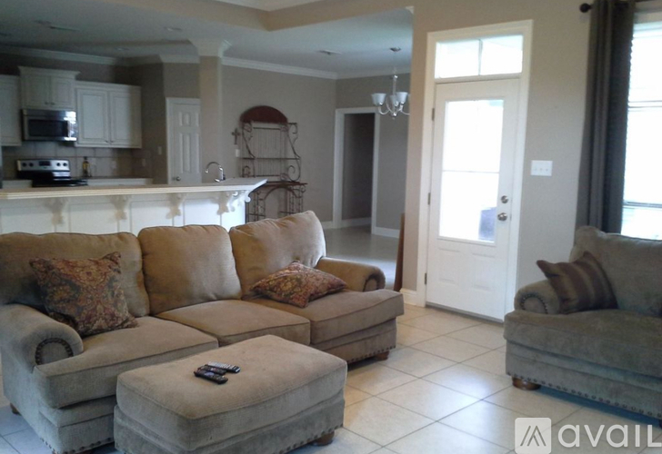 A living room with a couch and ottoman in front of a kitchen area.