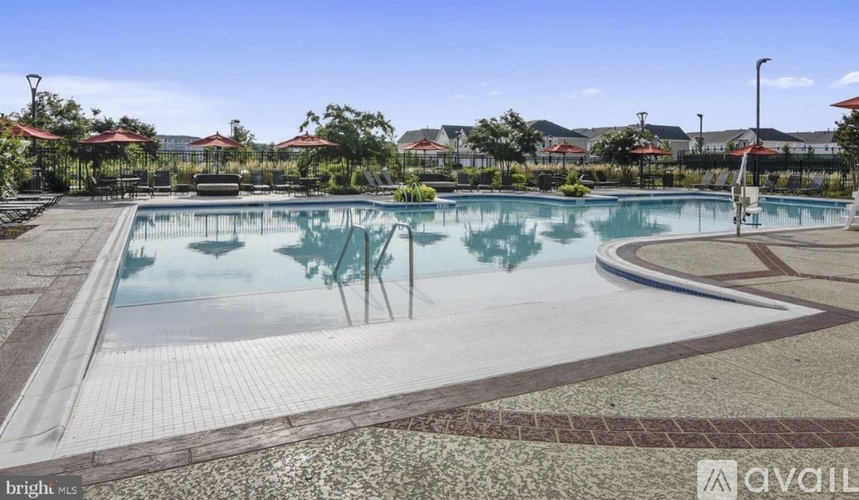 A large outdoor swimming pool surrounded by a tiled patio and lush greenery.