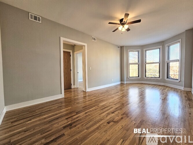 A spacious room with wooden flooring and a ceiling fan.