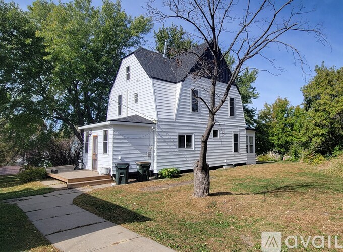 A white house with a black roof and a tree in front of it.