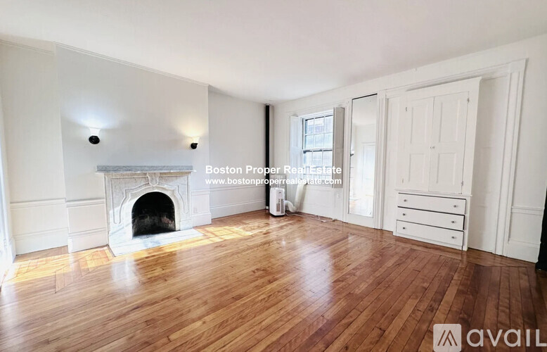 A spacious room with wooden floors and a fireplace.