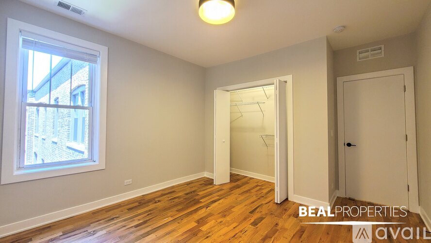 A room with wooden floors and a window showing a view of a building outside.