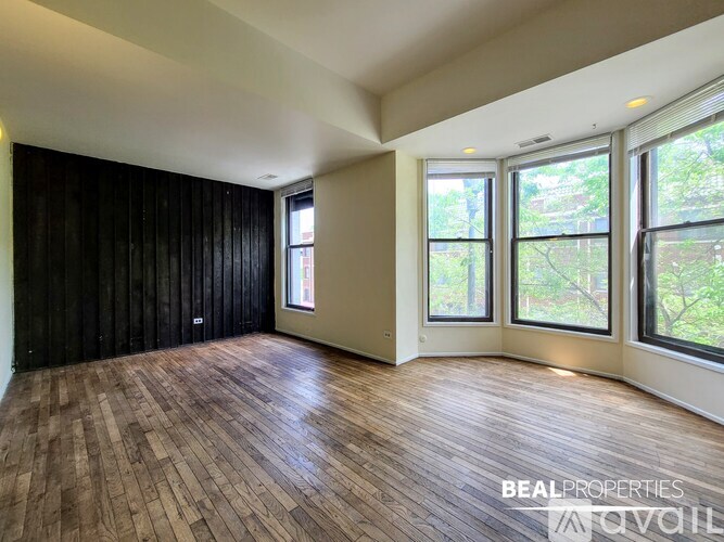 A spacious room with wooden flooring and large windows.