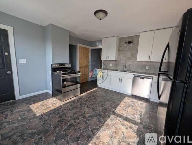A kitchen with a black refrigerator and a stone floor.