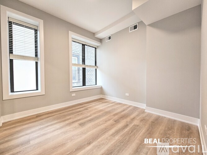 A spacious room with wooden flooring and two windows.