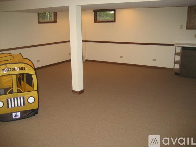 A yellow toy bus is in a room with brown carpeting.