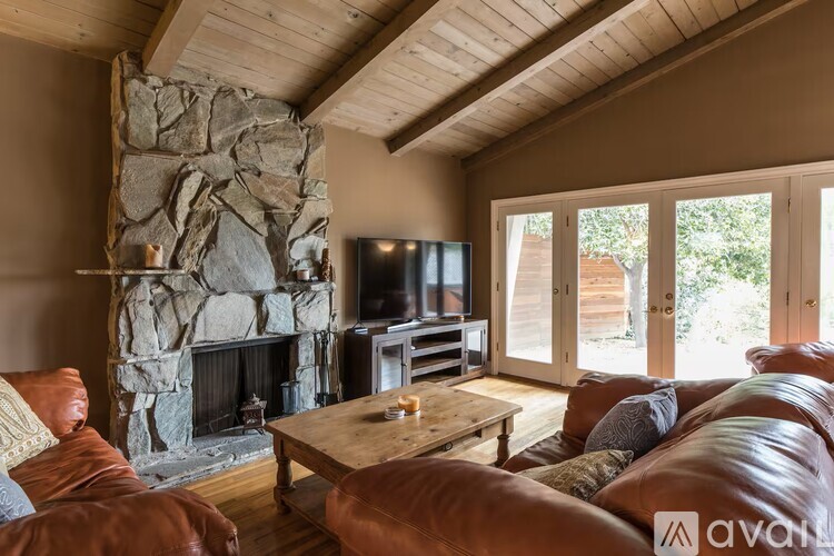A living room with a stone fireplace and a wooden ceiling.
