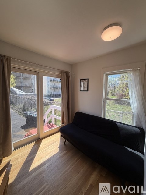 A living room with a black couch and a window overlooking a backyard.