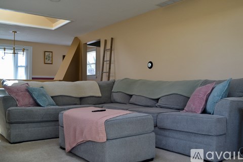 A living room with a grey couch and a pink blanket on it.
