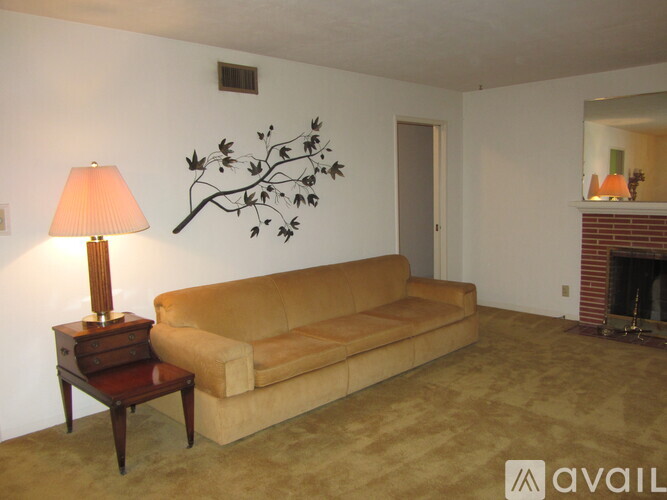 A living room with a tan couch, a lamp on a small table, and a fireplace.