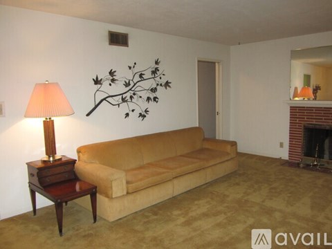 A living room with a tan couch, a lamp on a small table, and a fireplace.