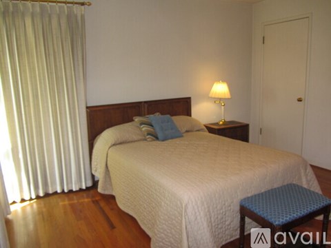 A bedroom with a bed, a nightstand with a lamp, and a window with curtains.