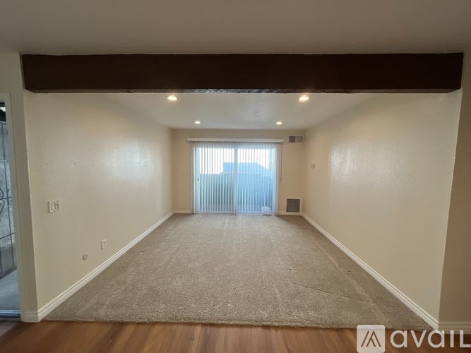 A spacious room with a carpeted floor and a window with blinds.
