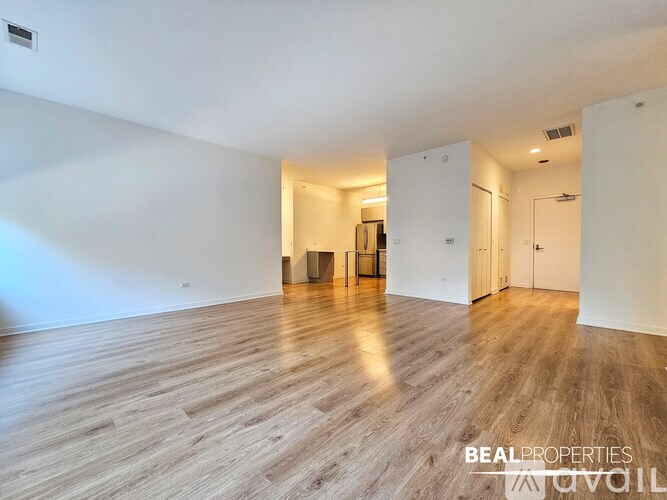A spacious room with wooden flooring and white walls, with a doorway leading to another room.