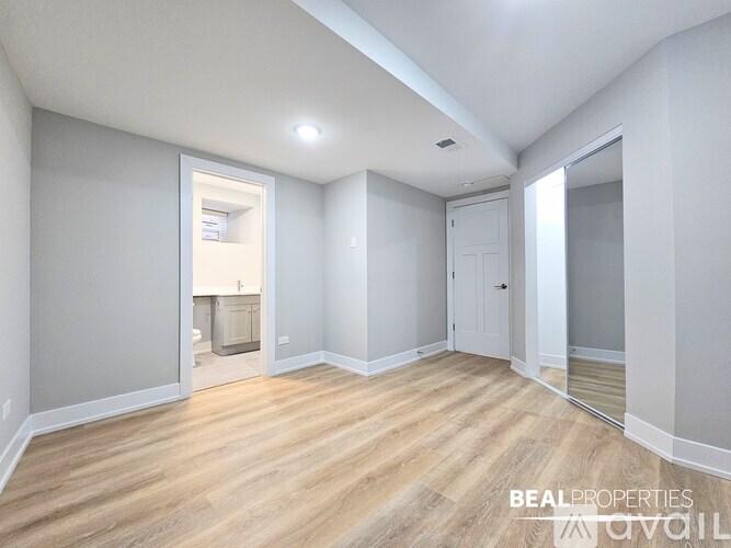 A spacious room with wooden flooring and white walls, with a doorway leading to another room.