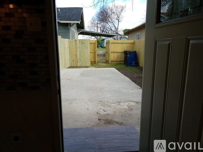 A view from inside a building looking out to a driveway and a fence.