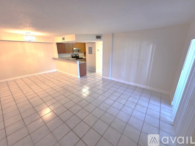 A spacious room with white tiled flooring and a kitchen area in the background.